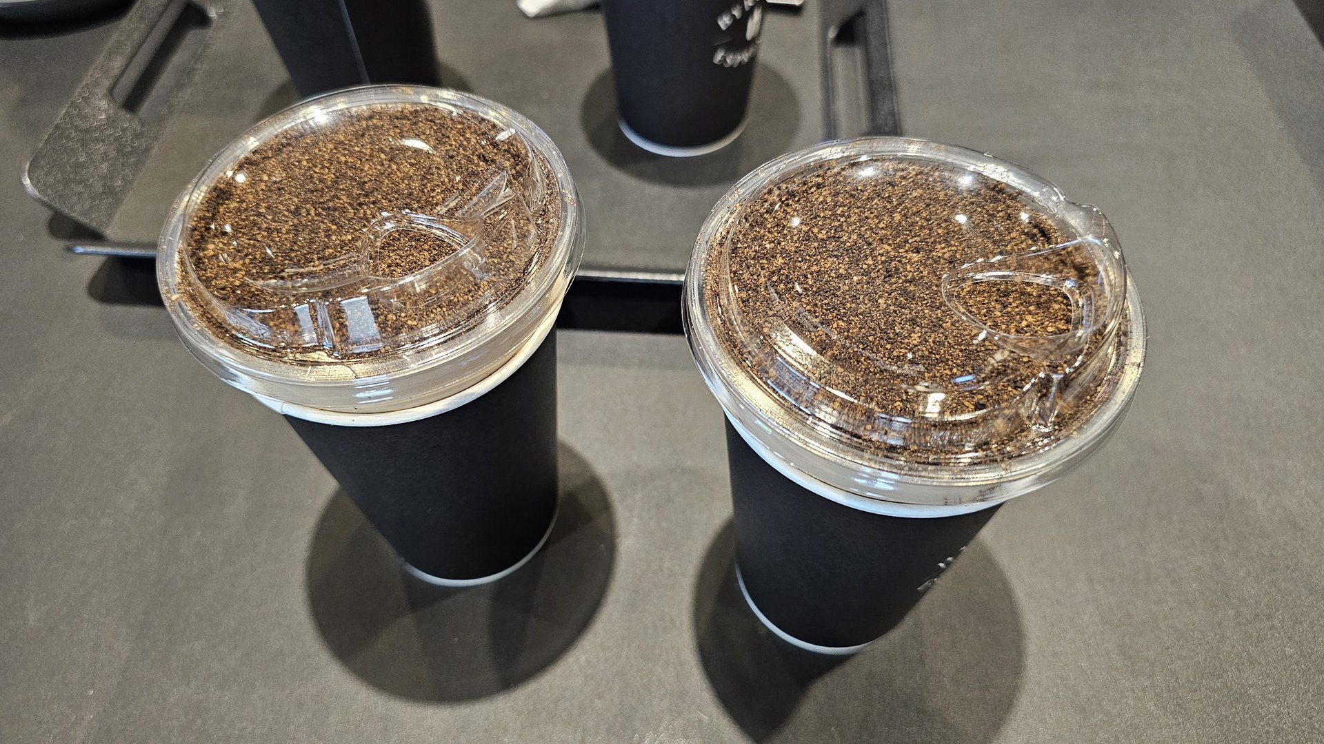 Overhead view of two signature iced drinks at Byronic Espresso with coffee crumble grounds covering black cup lids