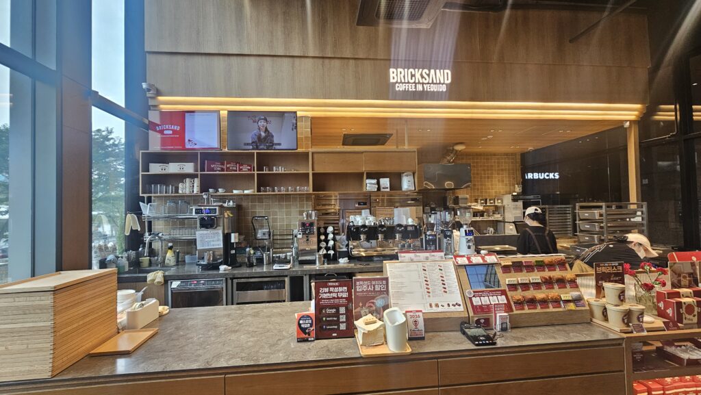 Counter notice board at Bricksand Coffee Yeouido showing review event promotion, building tenant discount, and Pass Order pickup zone signs