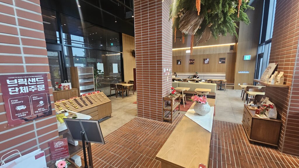Interior of Bricksand Coffee Yeouido with red brick pillars, wood tables, group order banner, and ceiling plant decorations