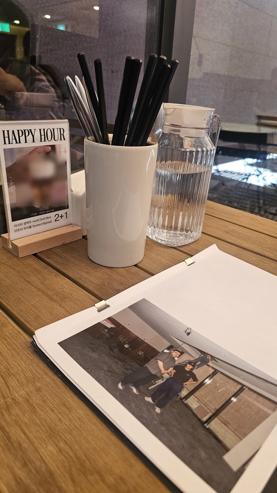 Table setup at Keebo Yeouido with utensil holder, water glass, and Happy Hour 2+1 promotion card