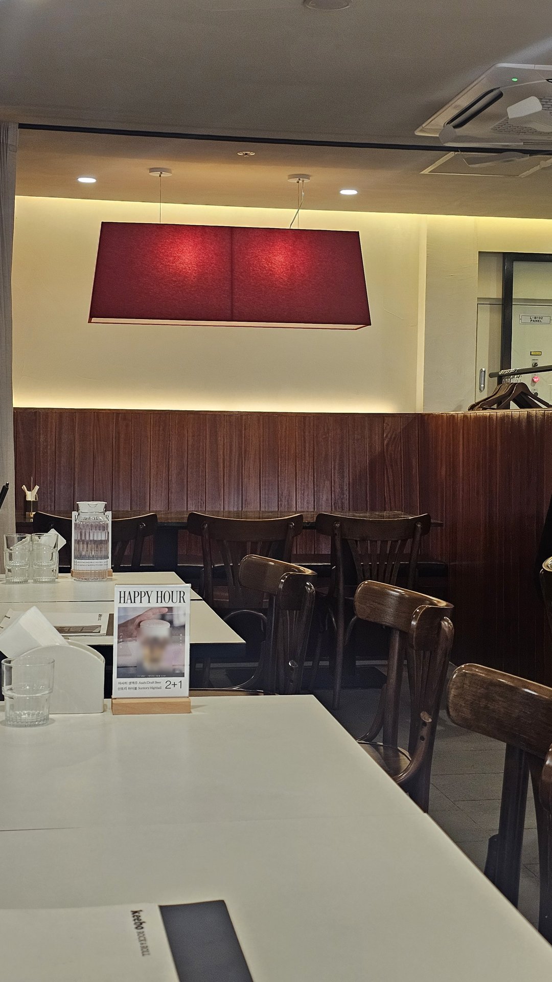 Interior wall at Keebo Yeouido with red textile artwork, dark wood booths, and Happy Hour signage
