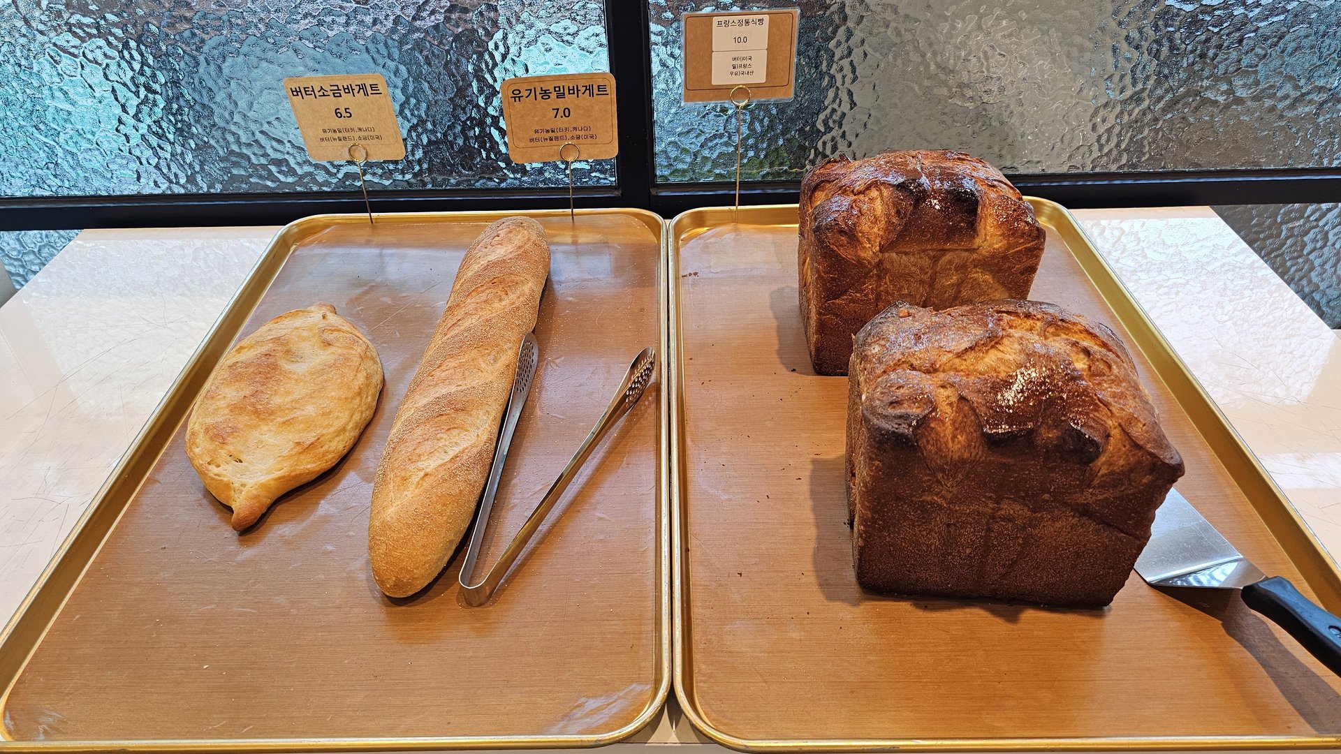 Baguette, ciabatta, and organic whole wheat hard bread loaves on display tray at Mochang-po Master Baker Cafe