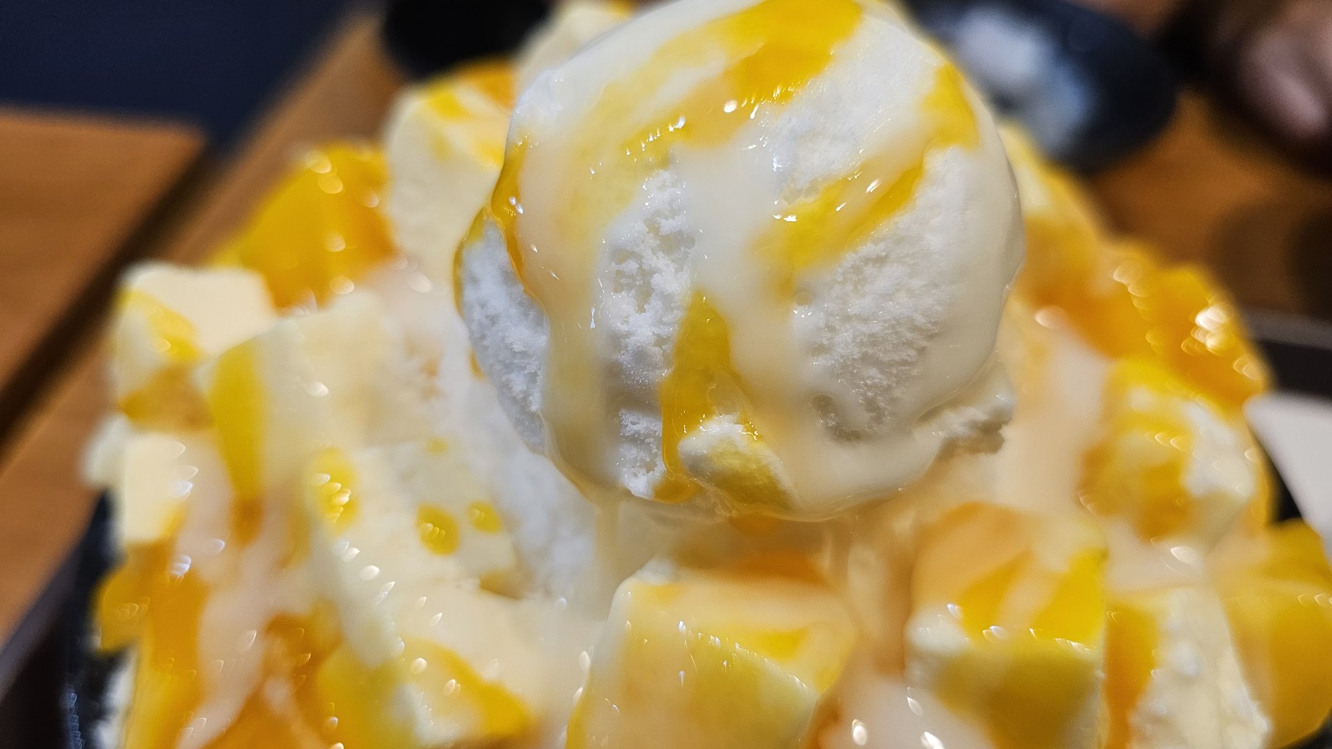 Extreme close-up of vanilla ice cream scoop on apple mango cheese bingsu with mango sauce melting