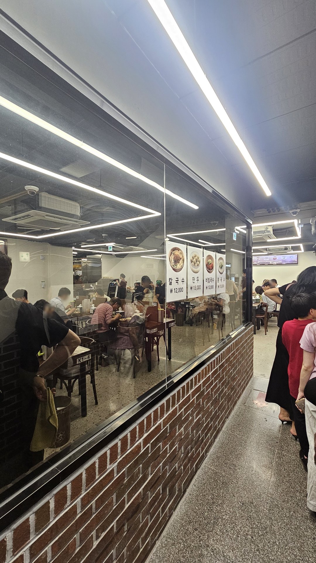 Interior view through glass window showing queue and menu price board at Myeongdong Gyoja