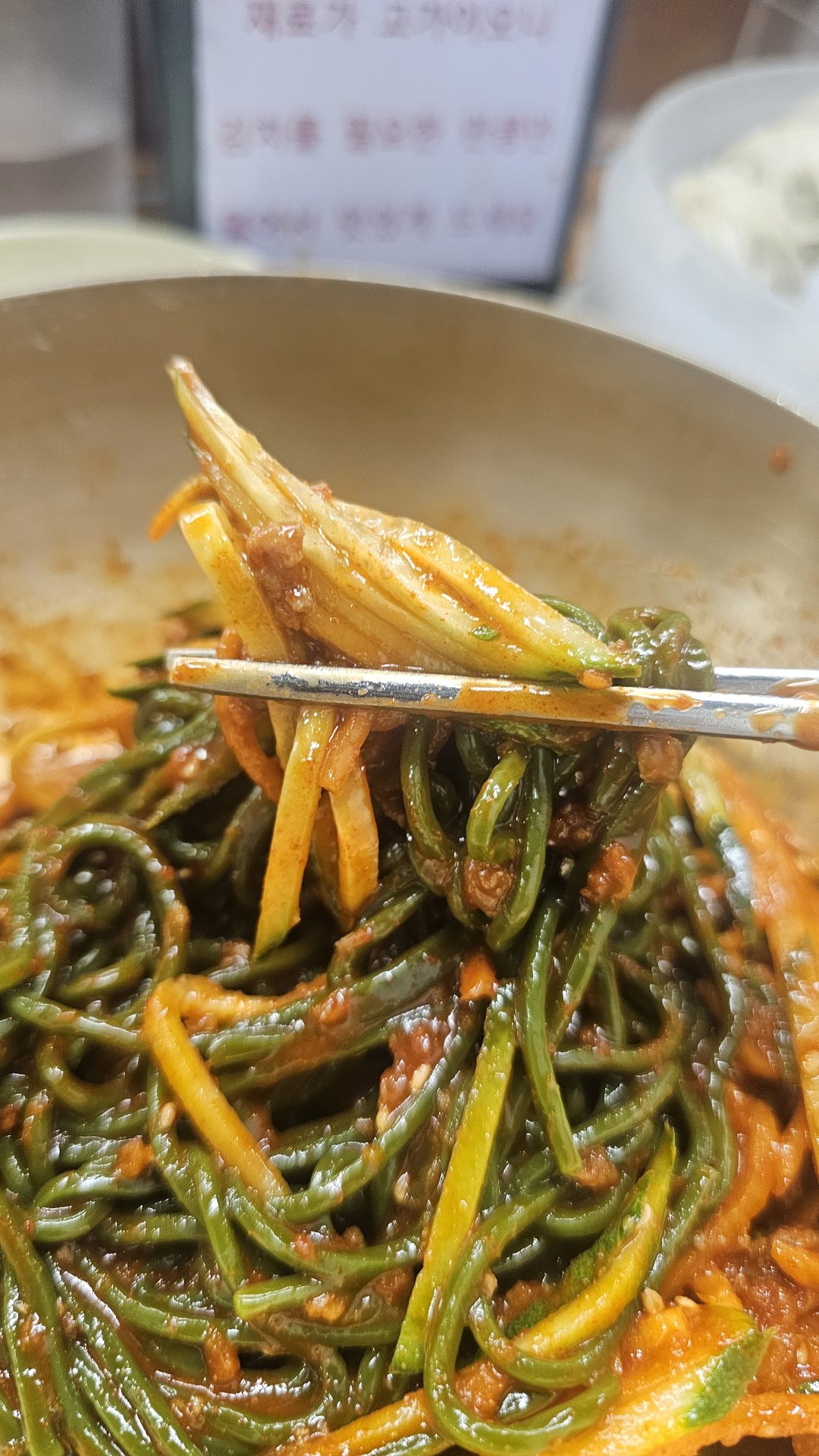 Chopsticks lifting bibim guksu cold noodles showing green and yellow strands