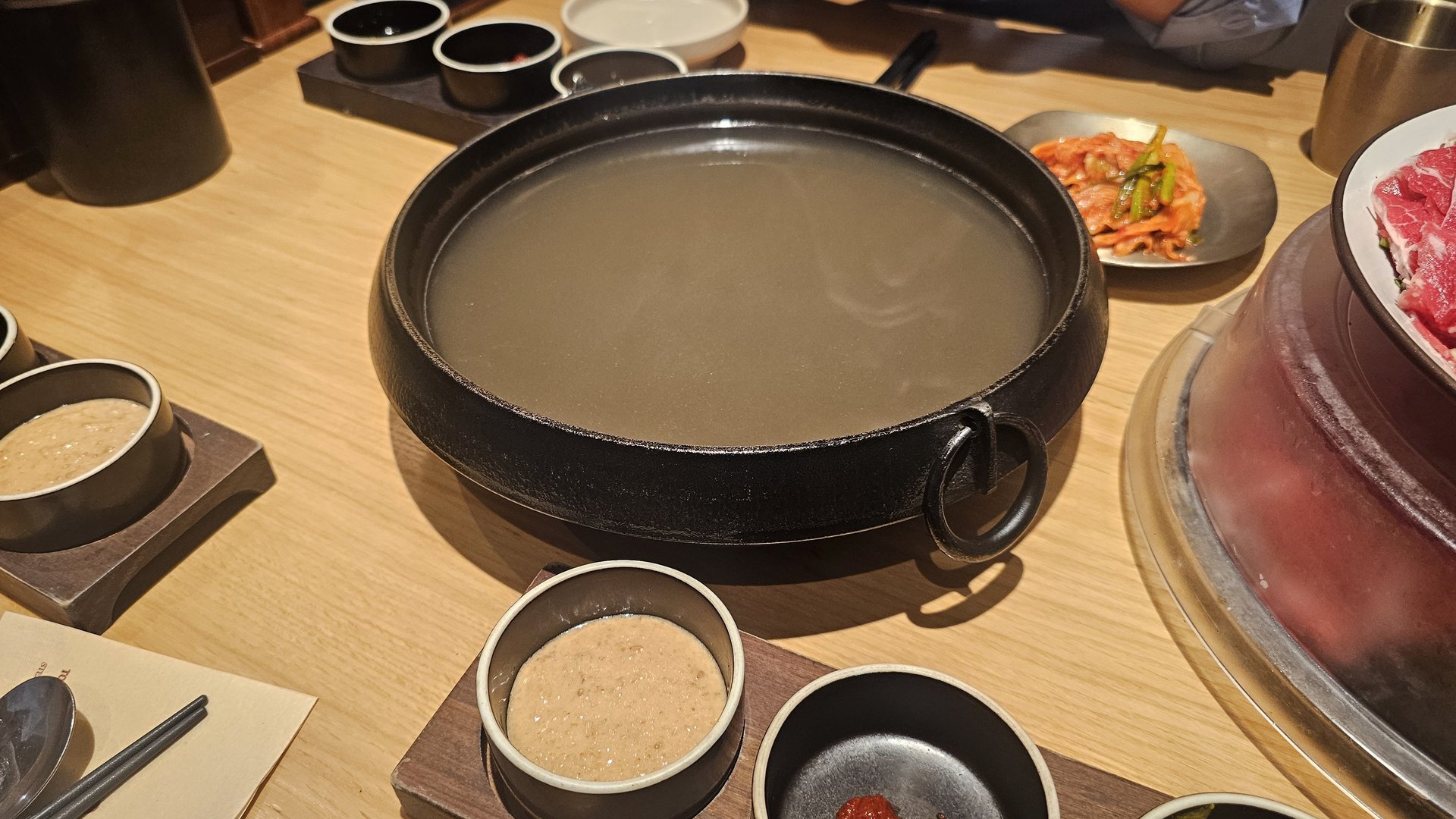Initial hot pot setup at Jeil Myeonso with clear broth in the pot and raw beef and kimchi waiting on the side