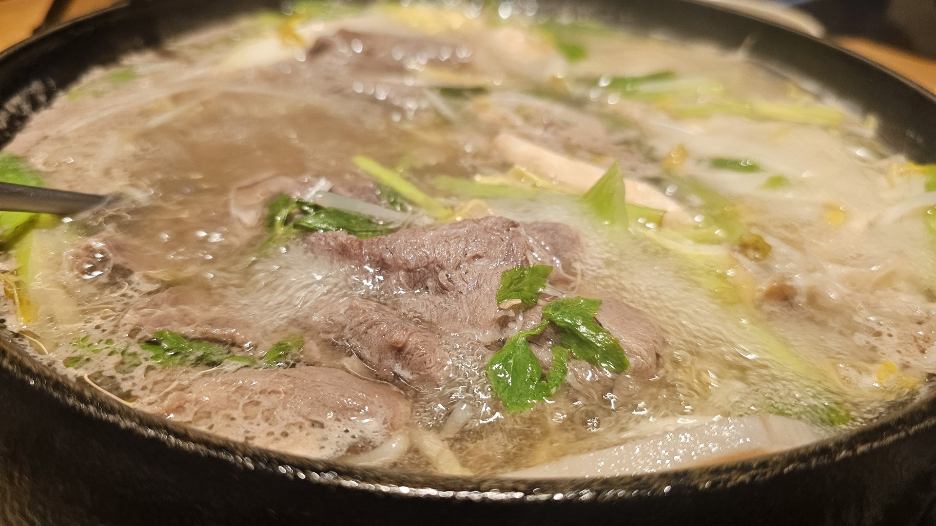 Black ingredient plate at Jeil Myeonso with the restaurant logo pick in the beef, showing beef, bean sprouts, lotus root, green chili, and perilla leaves