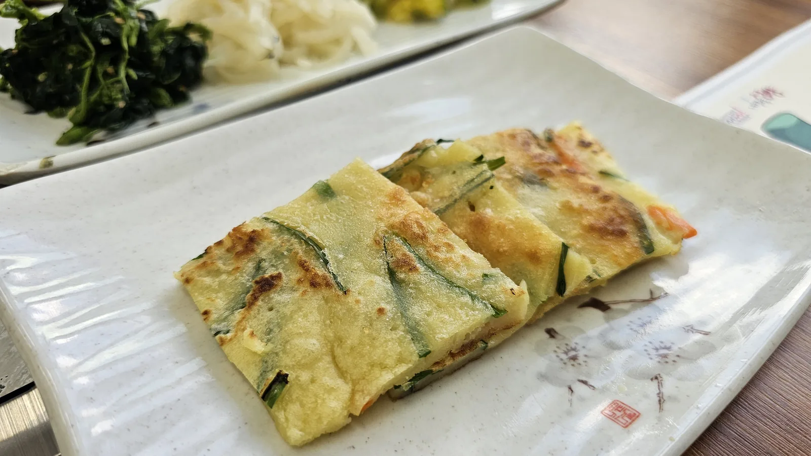 Vegetable jeon close-up at Nongbu Bapsang showing crispy Korean savory pancake with green onion and carrot pieces