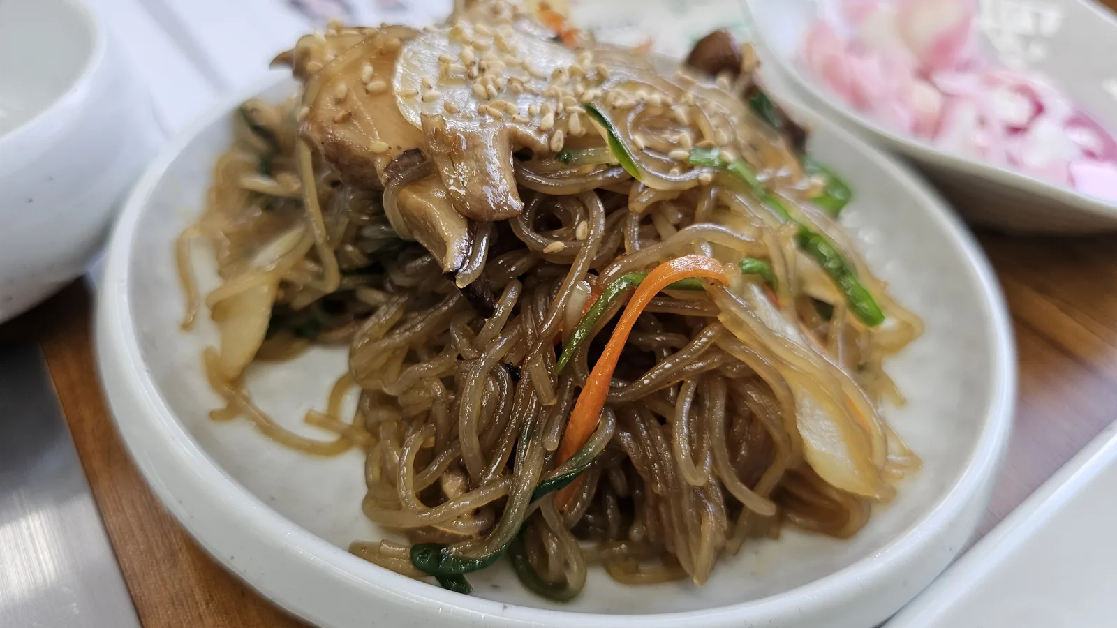 Japchae glass noodles close-up at Nongbu Bapsang with shiitake mushrooms, green onion, carrot, and sesame seeds
