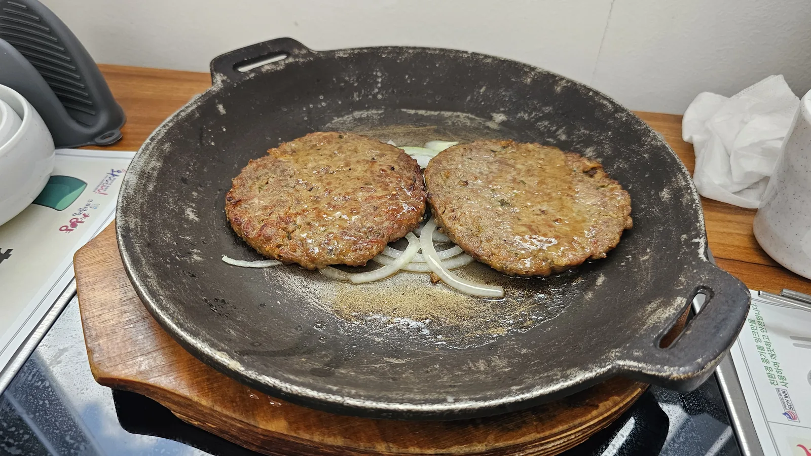 Goji berry tteok-galbi grilling on cast iron pan at Nongbu Bapsang with two round meat patties on a bed of onions